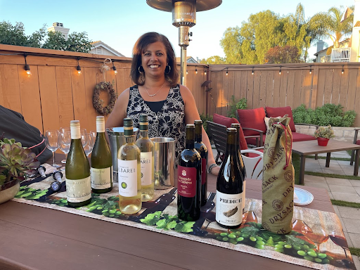 An evening in-home wine tasting on a string-lit patio, the host behind a table set with red and white wines and glasses.